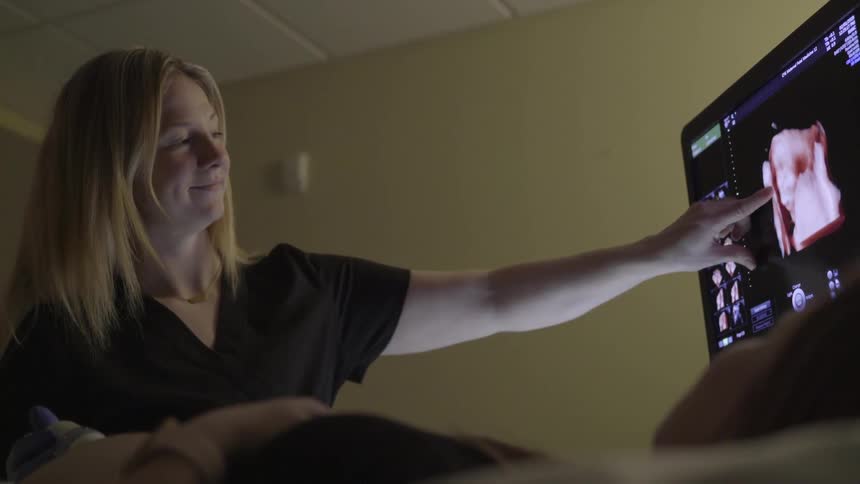 An ultrasound technician shows an expectant mother her ultrasound on a computer screen