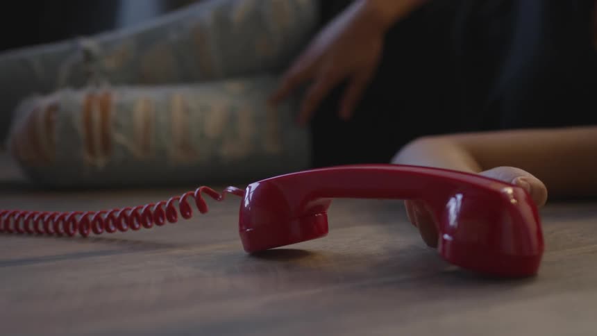 The woman in ripped and stylish jeans drops the red phone vintage phone as she collapses on the floor