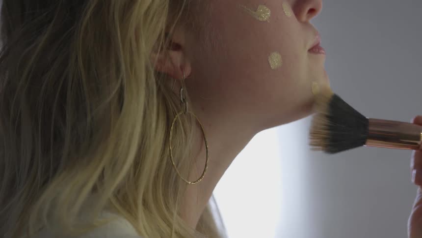 A woman applies makeup to her face with a brush