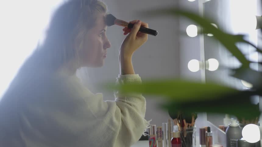A woman in front of a mirror applying makeup