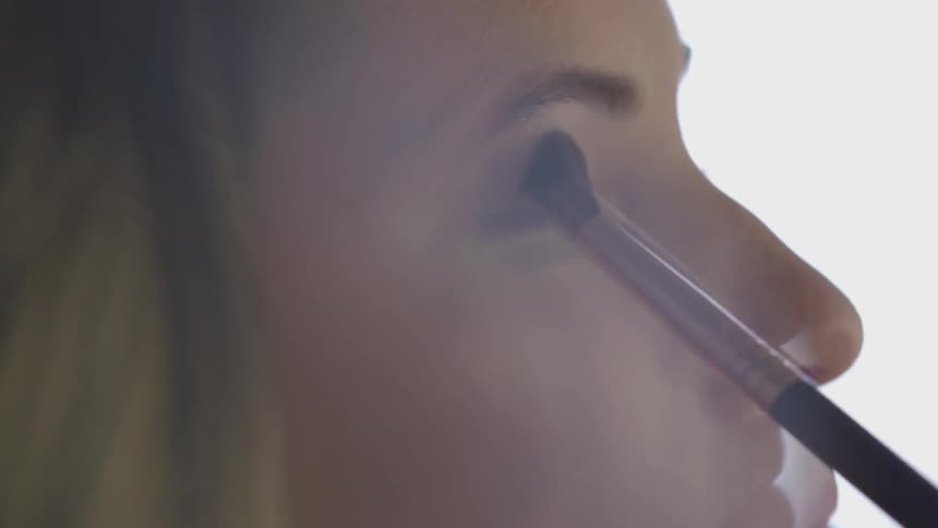 A young woman applies eye shadow using a brush
