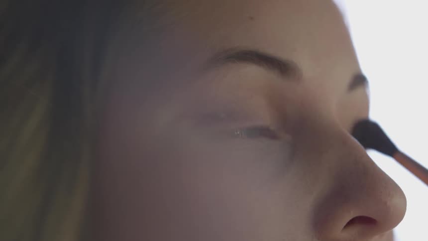 Woman applying makeup on her eyelids with a small brush