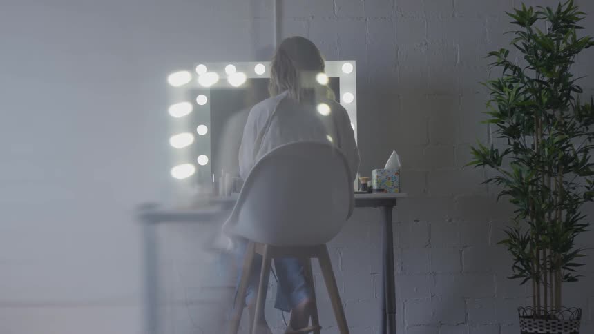 A woman sitting in a makeup studio putting on makeup