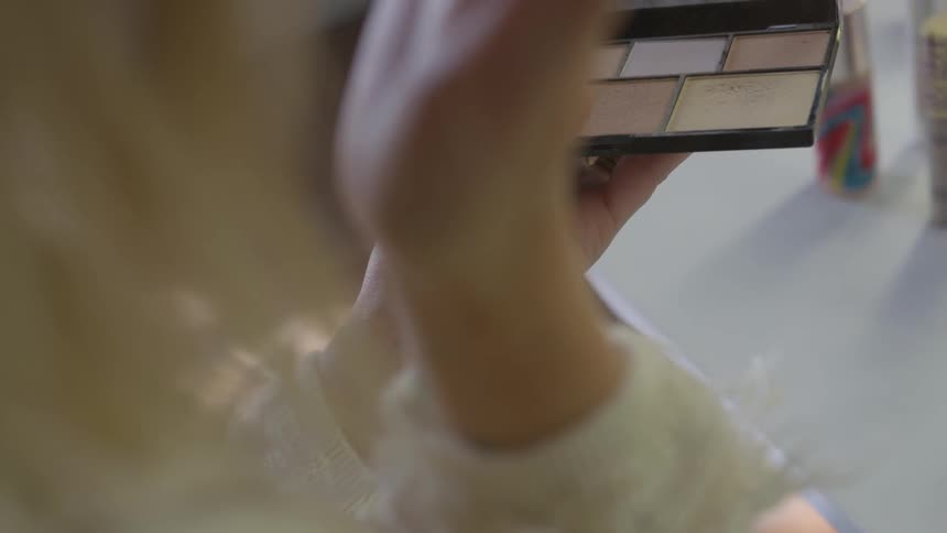 A woman holds a compact and applies makeup