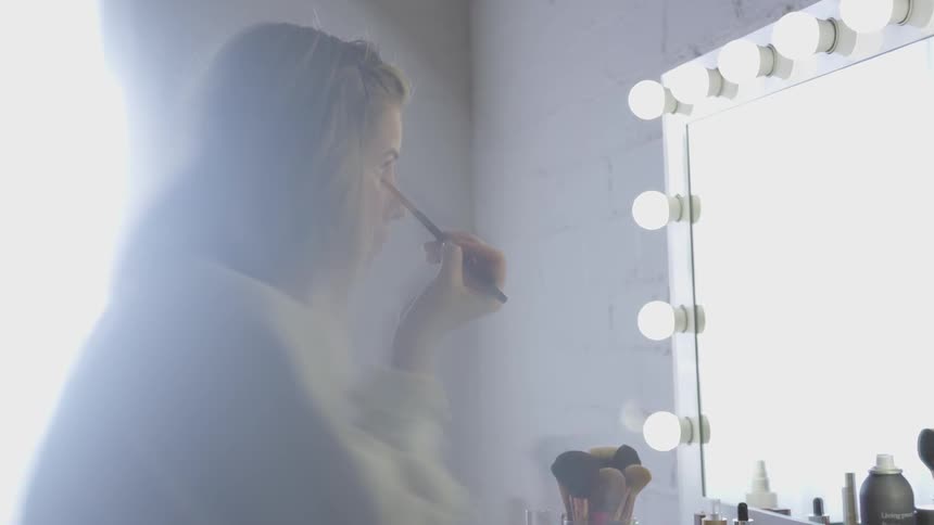 A woman is applying makeup and looking into a mirror