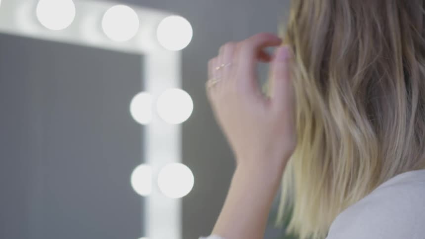 Woman sprays hair spray in hair while looking in a mirror