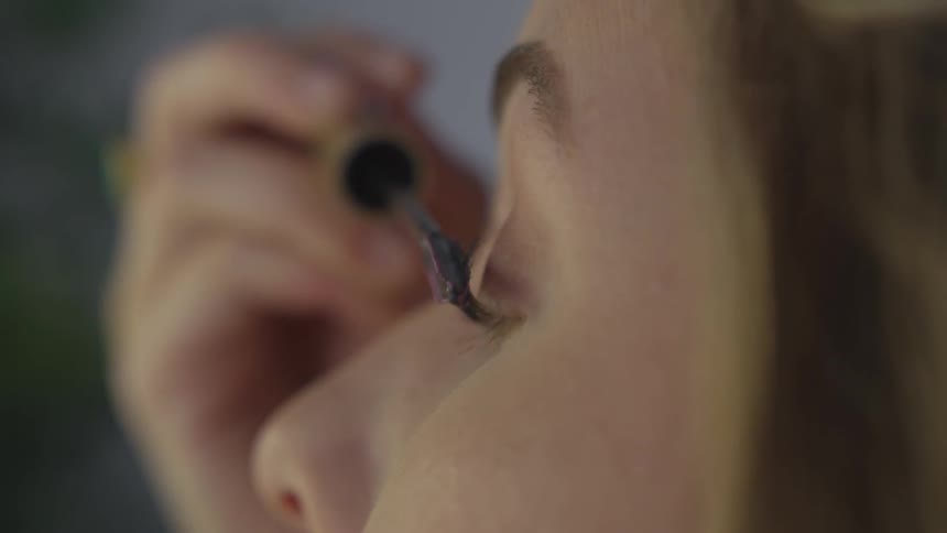 A woman puts mascara on