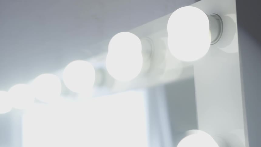 Camera looks closely at light bulbs around a mirror