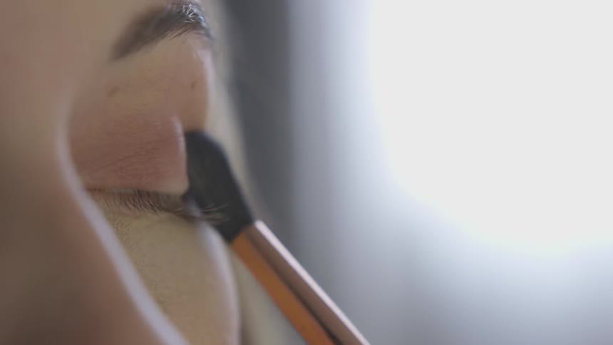 Woman makes makeup on eyelids with brush by day