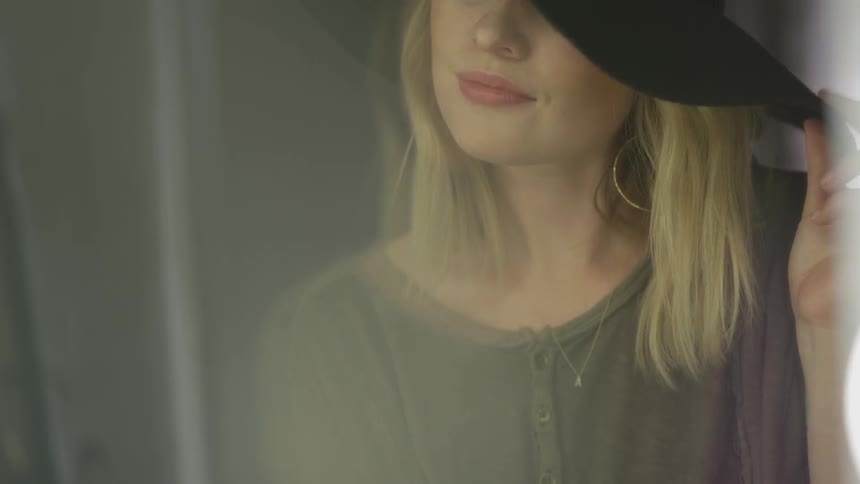Woman stands before mirror to adjust hat