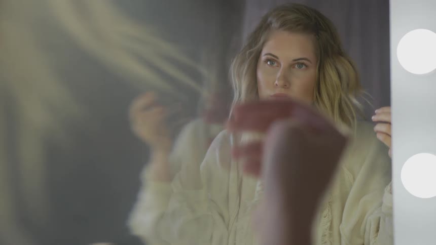 Blonde woman looks in mirror and touches hair indoors