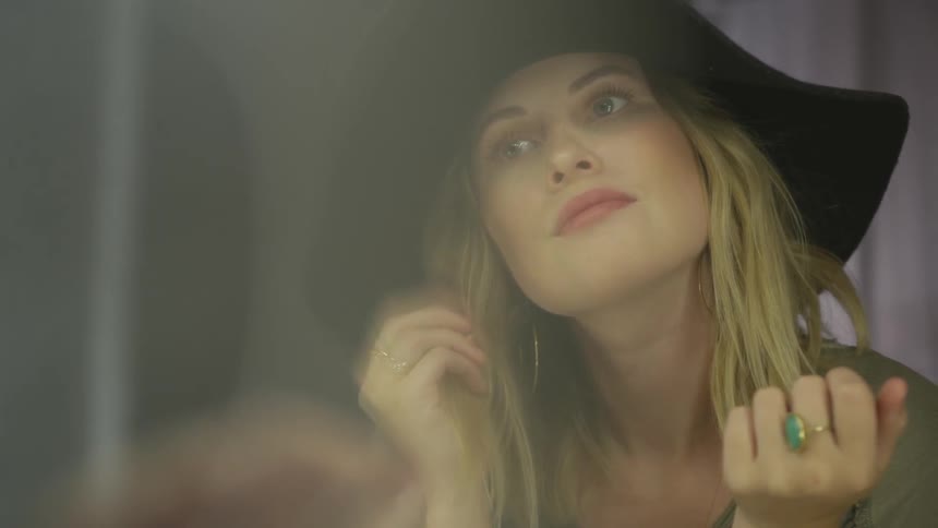 A blonde female in a floppy black hat twirling her hair