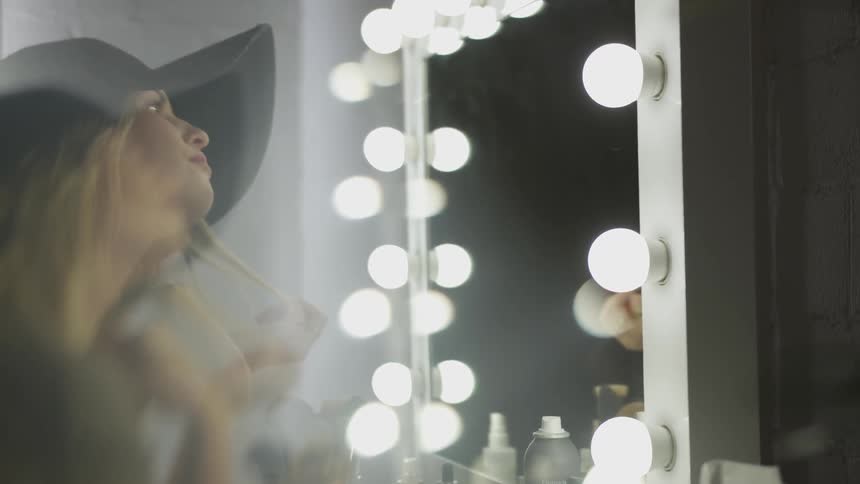 Woman wearing black wide hat looks in the mirror and smiles in room