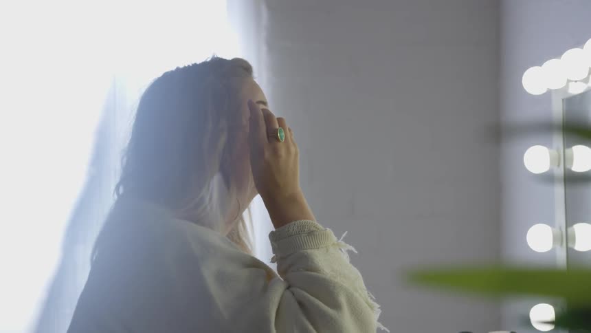 Woman applies mascara in front of vanity mirror