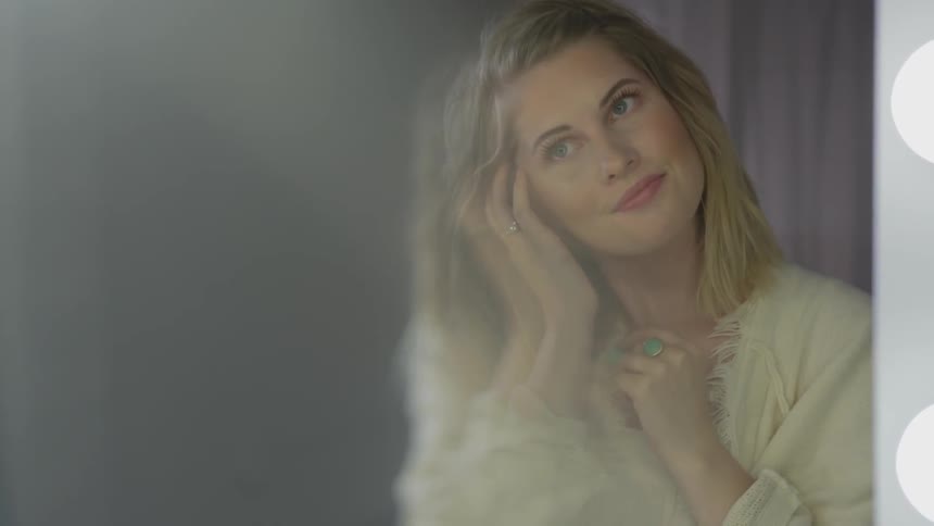 Blonde woman looks in mirror and smiles while touching hair indoors