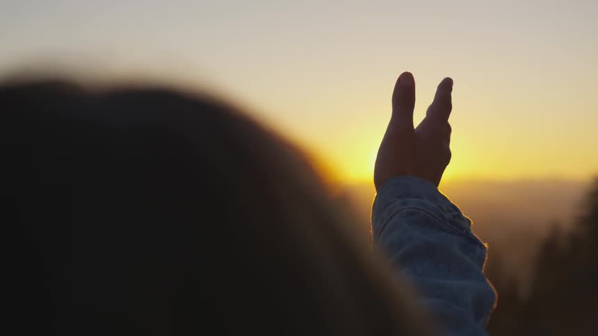Hands reaching out towards the sunset in the mountains