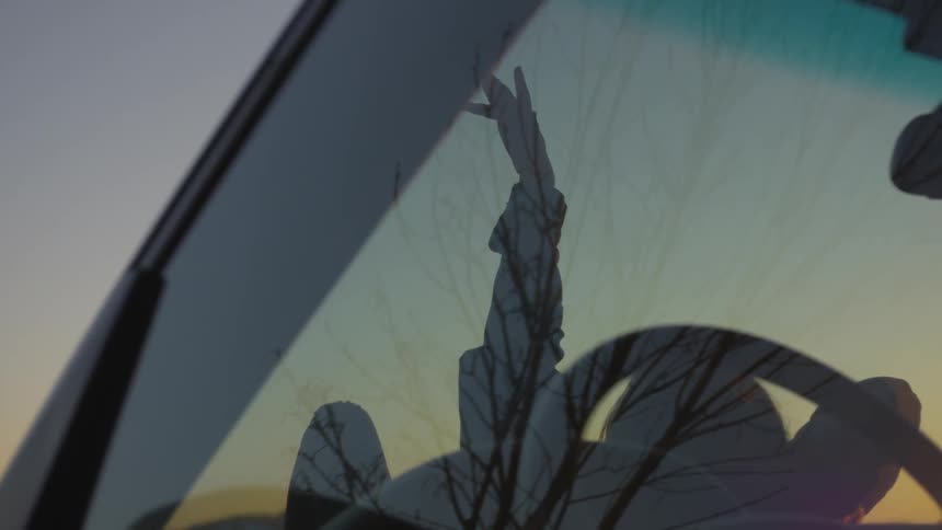 Person lays on car hood reaching toward sky