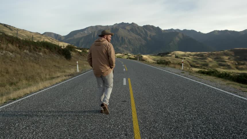 A bearded man walks along a two lane mountain road