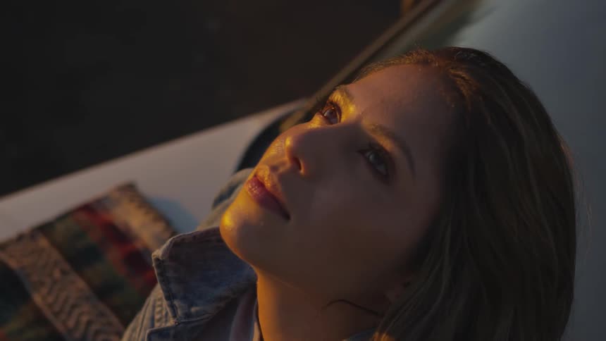 Woman sitting on the hood of a car looking up at the sky at sunset
