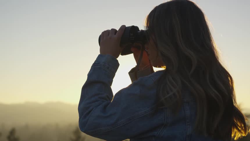 A woman uses binoculars in mountains at sunset