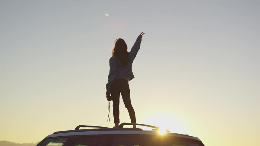 A woman is standing on top of a car outdoors