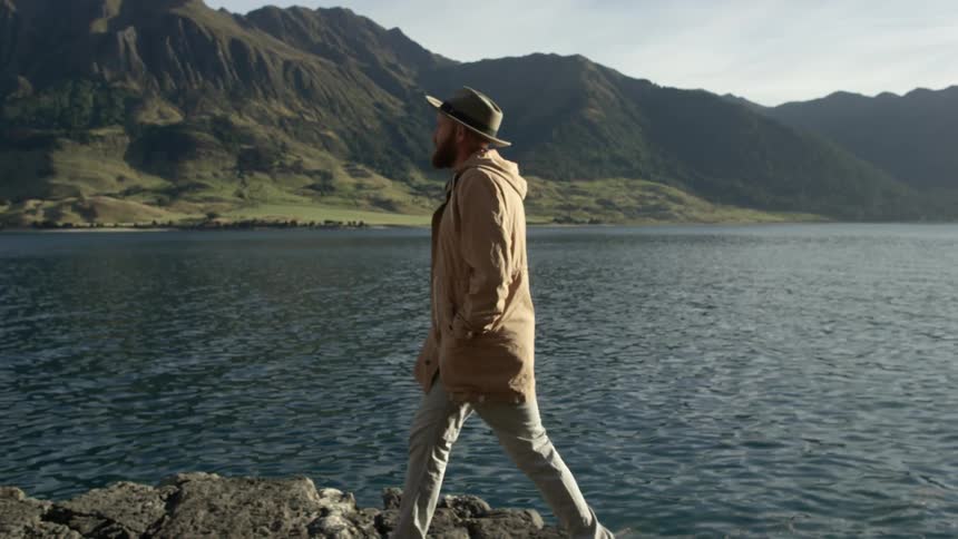 A man walks along some rocks by the shore on a sunny day