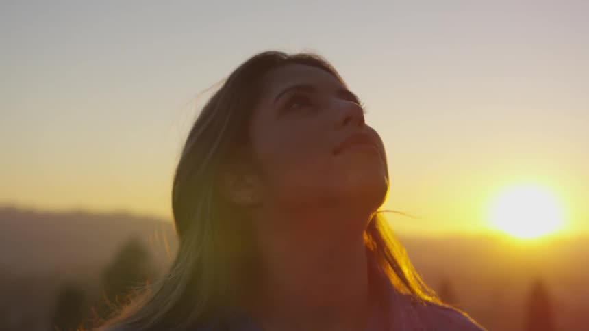 A woman is looking up outdoors while the sun sets