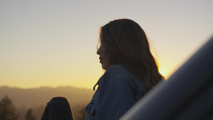 She is young about 30ish sitting on the hood apprehensively early in the morning or the end of day the trees look like people or the people trees