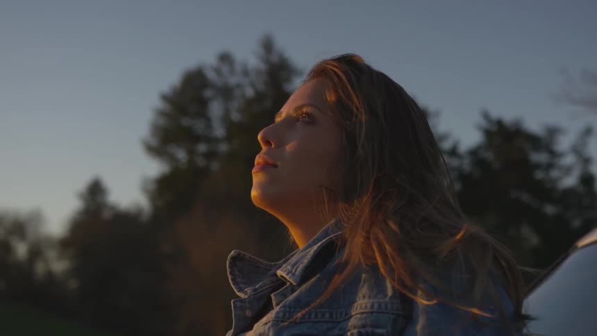 A woman is resting outside on her car hood and looking up