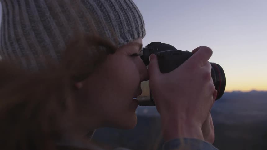 Woman lifts camera to take a photograph outdoors at sunset