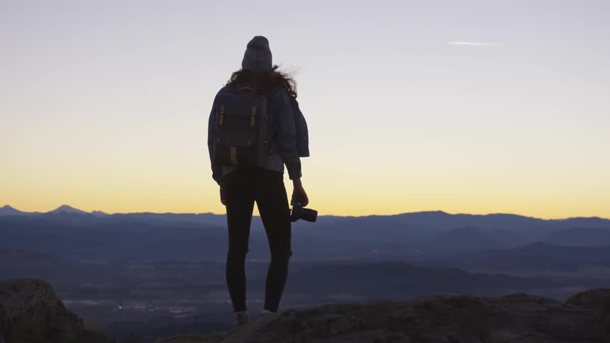 A woman holds a camera while looking over the horizon