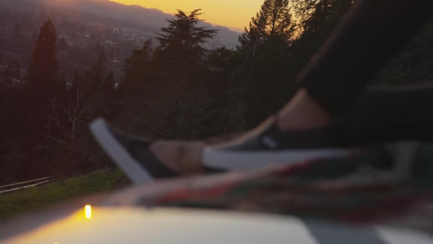 A woman sits in front of fir trees as the sun sets