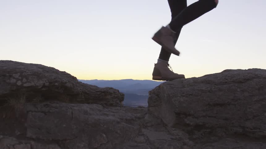 A woman hops across rocks during a hike