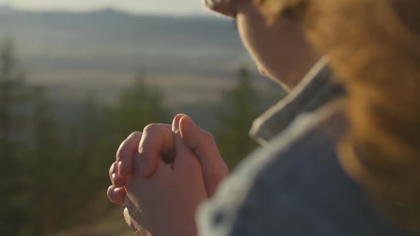 Woman praying on a hill at sunset
