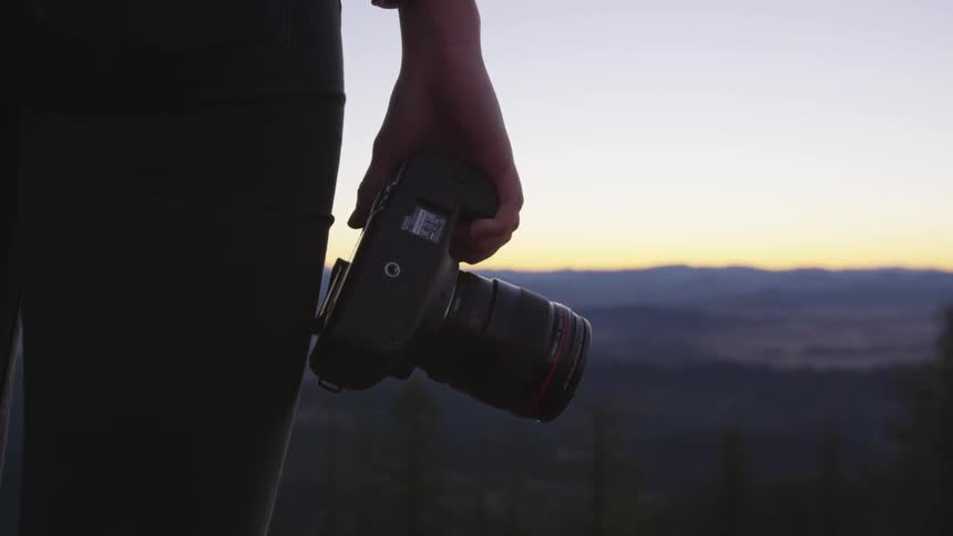 Man holding a camera while standing at a hill looking at the horizon