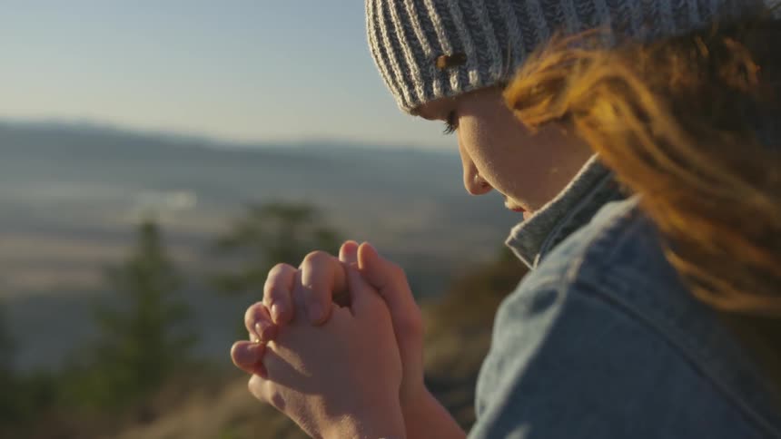 Her hands are together her head is bowed in prayer she is alone on a mountain top