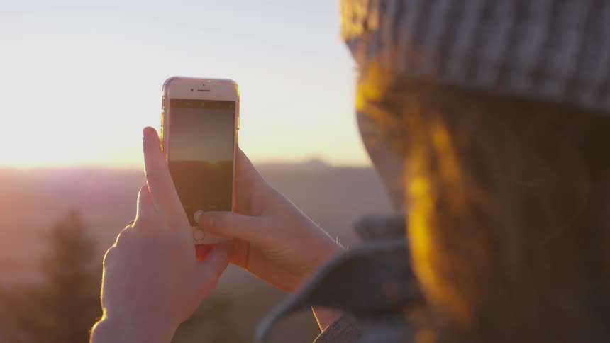 A woman is taking a picture of the horizon with a cell phone