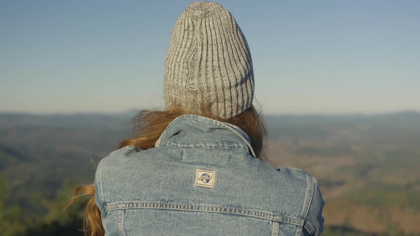 A woman wearing a hat stands elevated looking at the vast horizon