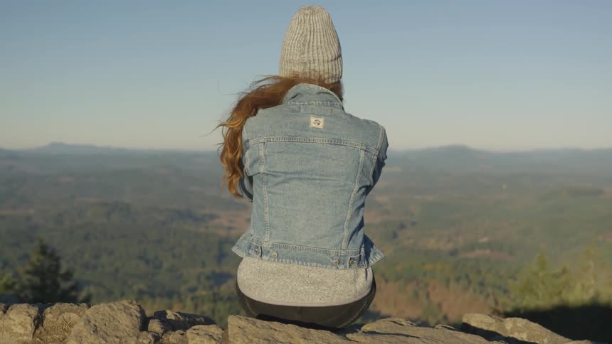 A woman sits on a rock ledge and looks out at the view