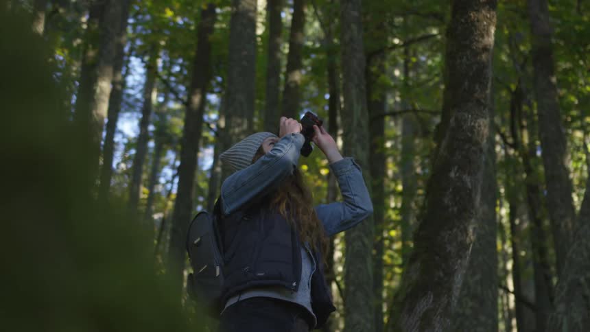 A woman points a camera to the sky while in the woods