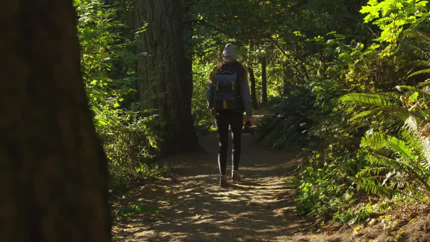 White person hiking in the middle of a forest while holding a camera