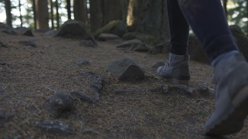 A woman walking through the woods over small rocks