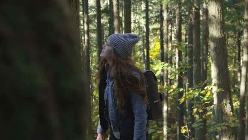 Female wearing a beanie and a backpack hiking through the forest