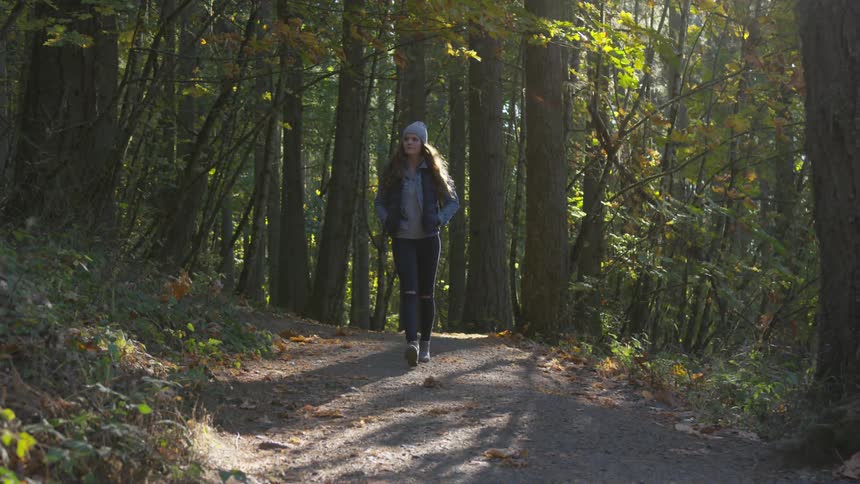 A woman wearing a hat walking through the woods