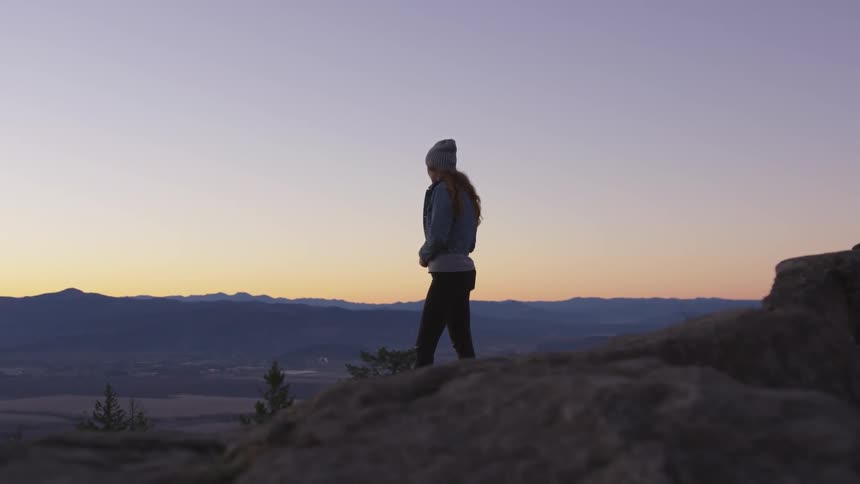 Woman standing on a hill looking at sunset