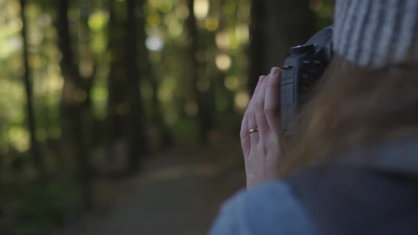 A woman holds up a camera to take a picture in the woods