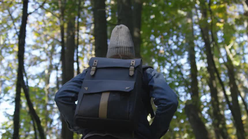 They are walking looking up at the trees with a backpack it is a sunny day