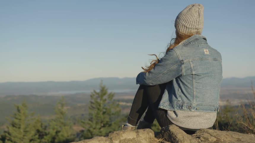 Woman sitting at rocks contemplating the horizon at the top of a hill