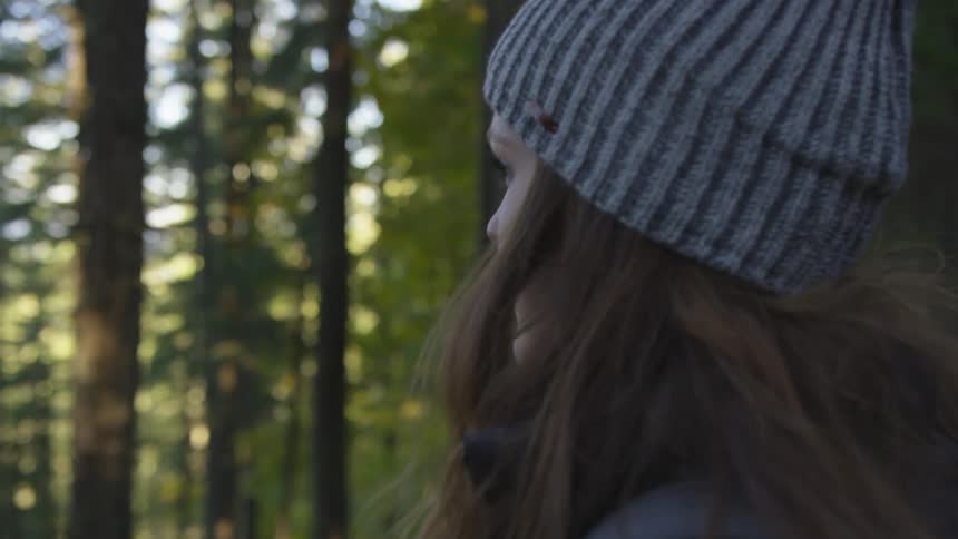 Woman with long dark hair wearing a beanie looking out into the forest