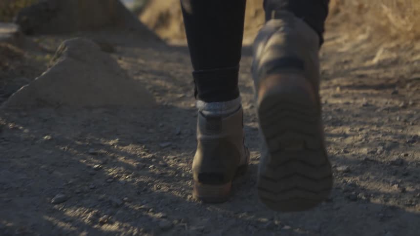 A person wearing boots walks along a path through the wilderness